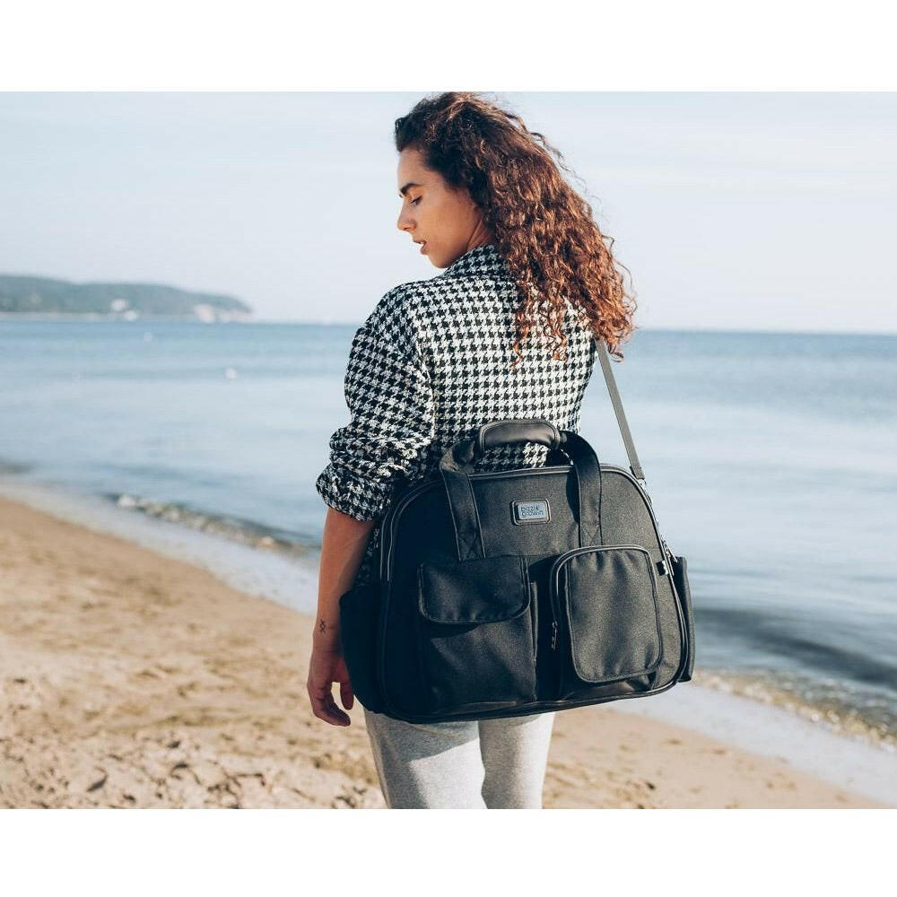Bizzi Grownin Travel Crib Changing Bag - The POD® (Chelsea Black) - lifestyle image, showing the bag being carried using the removable and adjustable shoulder strap